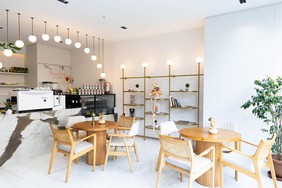 AllSunray içindeki kafe alanı; ahşap masalar, rattan sandalyeler ve altın rengi raflar